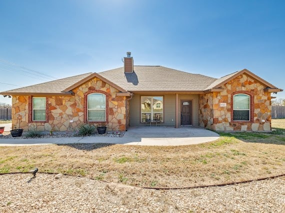 view of front of property with stone siding, a patio, a chimney, and a front lawn