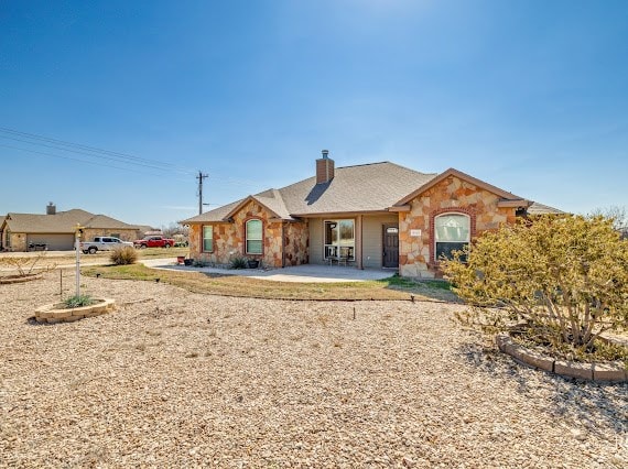 ranch-style house featuring stone siding, a patio area, and a chimney