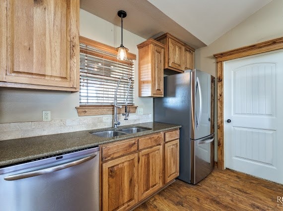 kitchen with lofted ceiling, stainless steel appliances, a sink, hanging light fixtures, and dark wood-style floors