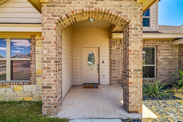 property entrance featuring brick siding and a shingled roof