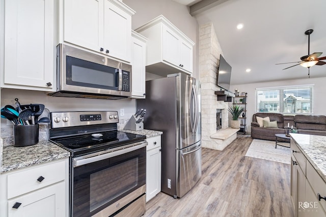 kitchen with lofted ceiling with beams, open floor plan, appliances with stainless steel finishes, light wood-type flooring, and a large fireplace