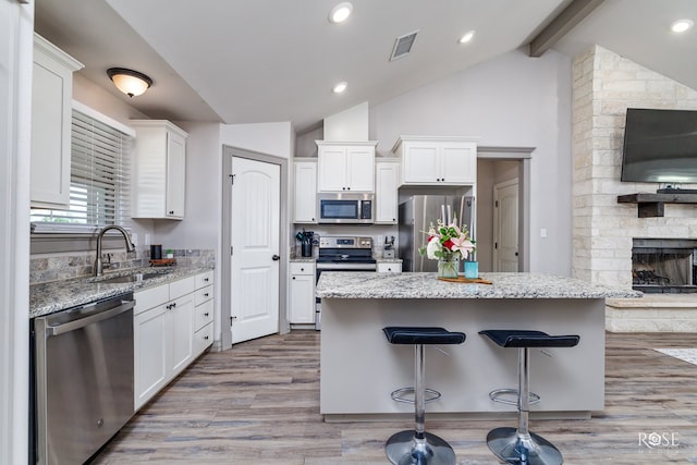 kitchen featuring a kitchen bar, a sink, lofted ceiling with beams, white cabinetry, and appliances with stainless steel finishes