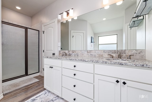 full bathroom featuring a shower stall, wood finished floors, double vanity, and a sink