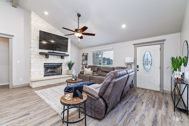 living area featuring baseboards, a stone fireplace, wood finished floors, and a ceiling fan