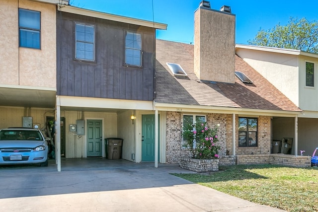 townhome / multi-family property featuring a carport, a front yard, a chimney, a shingled roof, and driveway