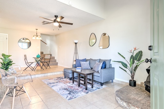 tiled living area featuring a textured ceiling, ceiling fan with notable chandelier, baseboards, and stairs