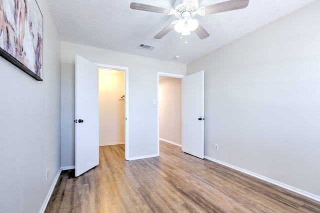 unfurnished bedroom with a textured ceiling, visible vents, wood finished floors, a walk in closet, and baseboards