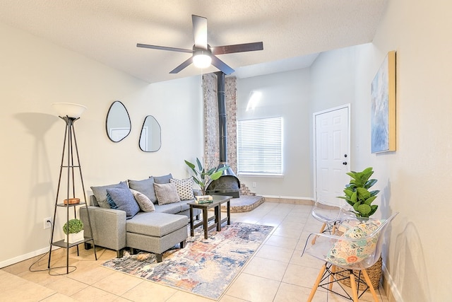 living area with light tile patterned floors, baseboards, a wood stove, a ceiling fan, and a textured ceiling