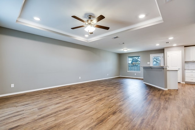 unfurnished living room with a tray ceiling, ornamental molding, ceiling fan, and light hardwood / wood-style flooring