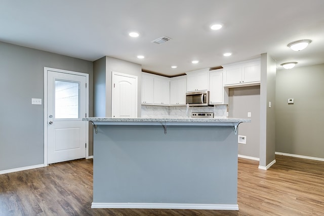 kitchen with light wood-type flooring, a center island with sink, white cabinets, and a breakfast bar