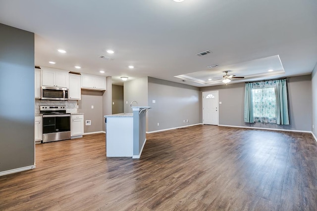 kitchen with appliances with stainless steel finishes, tasteful backsplash, white cabinets, a raised ceiling, and hardwood / wood-style floors