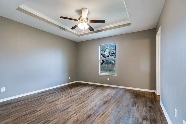 empty room with a tray ceiling, dark wood-type flooring, and crown molding