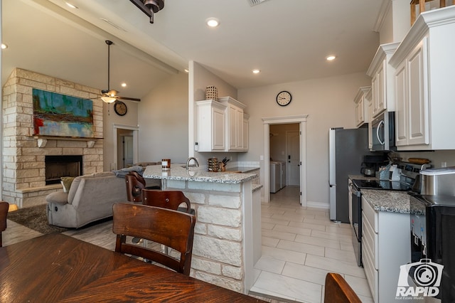 kitchen with light tile patterned flooring, appliances with stainless steel finishes, a fireplace, white cabinets, and light stone counters