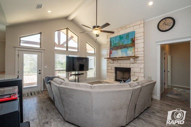 living room featuring ceiling fan, high vaulted ceiling, dark hardwood / wood-style flooring, a stone fireplace, and beamed ceiling