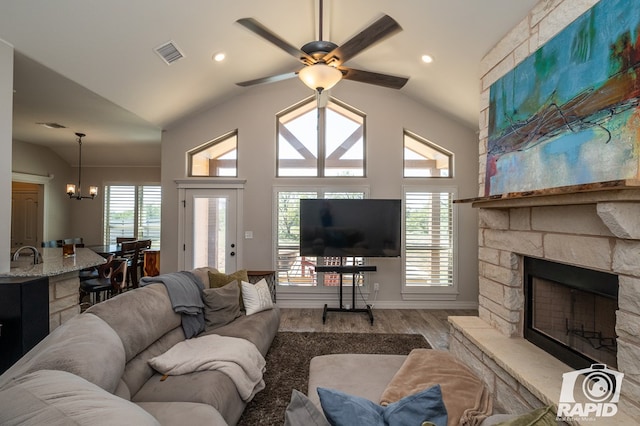 living room with lofted ceiling, a stone fireplace, sink, light wood-type flooring, and ceiling fan with notable chandelier