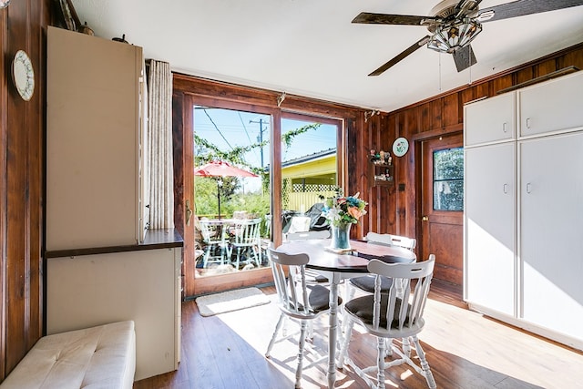 dining area with ceiling fan, light hardwood / wood-style floors, and wood walls