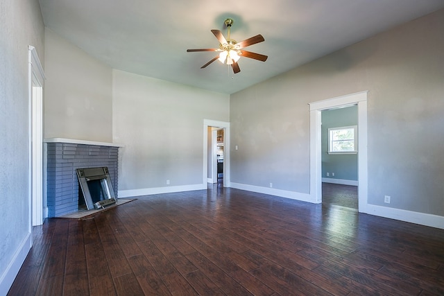 unfurnished living room with a brick fireplace, dark wood-type flooring, and ceiling fan