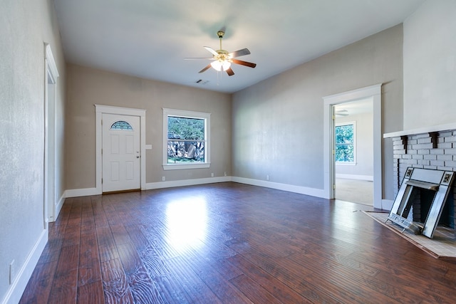 unfurnished living room with dark hardwood / wood-style flooring, a brick fireplace, a wealth of natural light, and ceiling fan