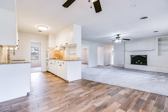 kitchen featuring white cabinets, light stone countertops, sink, and a brick fireplace