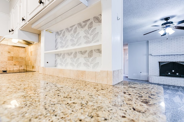 kitchen featuring white cabinetry, a brick fireplace, backsplash, ceiling fan, and a textured ceiling