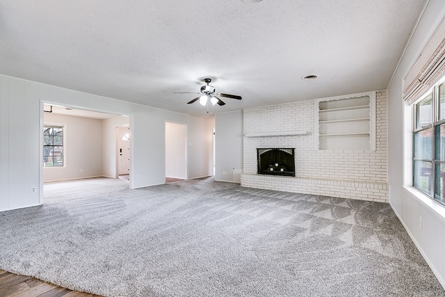 unfurnished living room featuring ceiling fan, carpet floors, a brick fireplace, and a textured ceiling