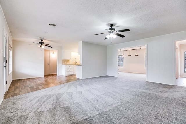 unfurnished living room with a textured ceiling, ceiling fan, light colored carpet, and sink