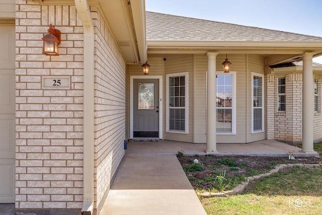 property entrance with covered porch, brick siding, and roof with shingles