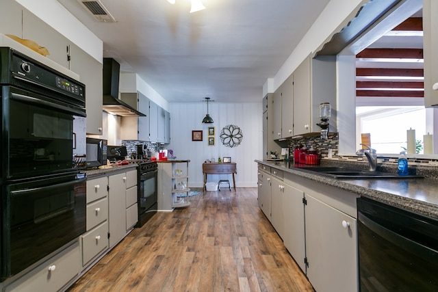 kitchen featuring sink, dark wood-type flooring, black appliances, decorative light fixtures, and wall chimney exhaust hood