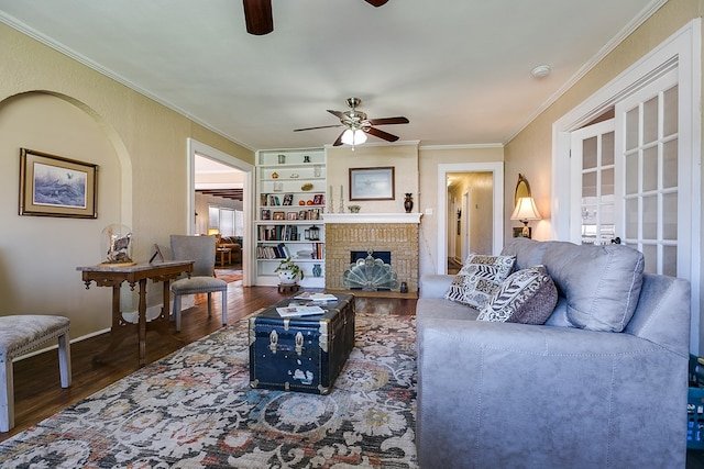 living room featuring crown molding, ceiling fan, hardwood / wood-style floors, a brick fireplace, and built in shelves