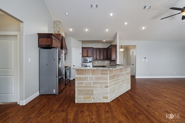 kitchen with appliances with stainless steel finishes, tasteful backsplash, ceiling fan, light stone counters, and dark wood-type flooring