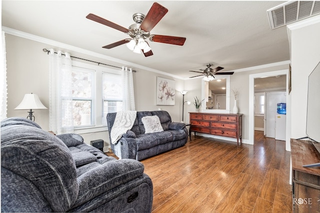 living area with baseboards, wood finished floors, visible vents, and crown molding