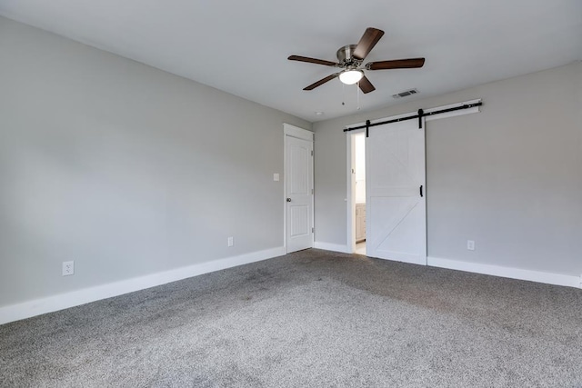 unfurnished room with a barn door, carpet, and ceiling fan