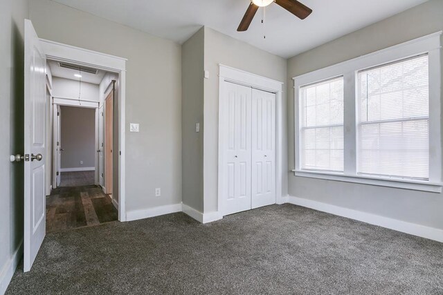 unfurnished bedroom featuring dark colored carpet, ceiling fan, and a closet