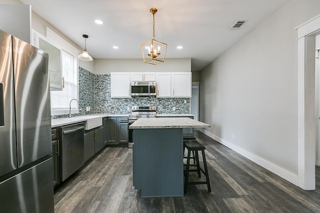 kitchen with white cabinetry, decorative light fixtures, appliances with stainless steel finishes, a kitchen island, and backsplash