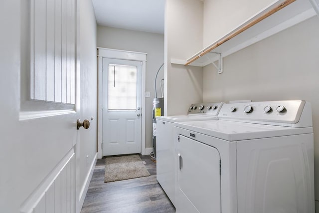 clothes washing area with hardwood / wood-style flooring, washing machine and dryer, and water heater