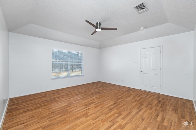 spare room with ceiling fan, lofted ceiling, a tray ceiling, and light hardwood / wood-style flooring