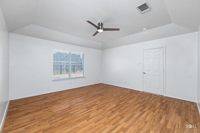 spare room with ceiling fan, lofted ceiling, a tray ceiling, and light hardwood / wood-style flooring