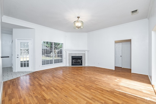 unfurnished living room featuring hardwood / wood-style flooring, crown molding, a notable chandelier, a textured ceiling, and a tiled fireplace