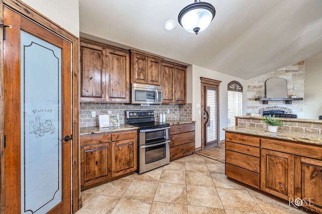 7738 Bison Trl, San Angelo, TX 76901 - kitchen with stainless steel appliances, lofted ceiling, decorative backsplash, a large fireplace, and light stone counters