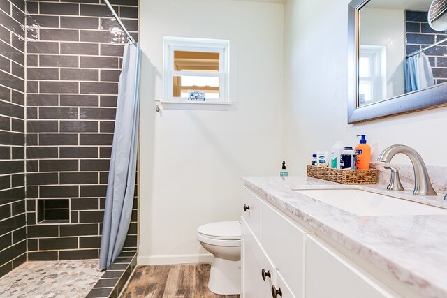 full bathroom with wood finished floors, vanity, baseboards, a tile shower, and toilet