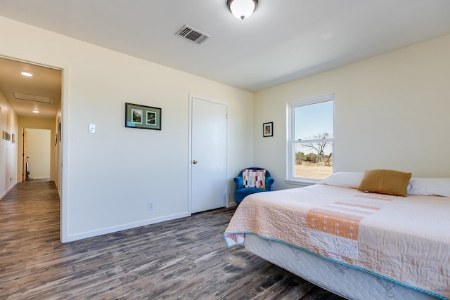 bedroom with visible vents, baseboards, attic access, and wood finished floors