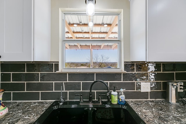 kitchen with white cabinets, a sink, dark stone counters, and tasteful backsplash