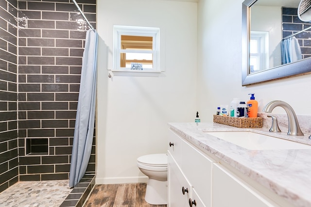 bathroom with vanity, wood finished floors, baseboards, tiled shower, and toilet