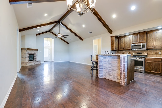 kitchen featuring open floor plan, appliances with stainless steel finishes, a kitchen bar, and brown cabinets