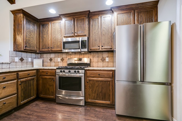 kitchen with appliances with stainless steel finishes, tasteful backsplash, light stone counters, and dark wood-style floors