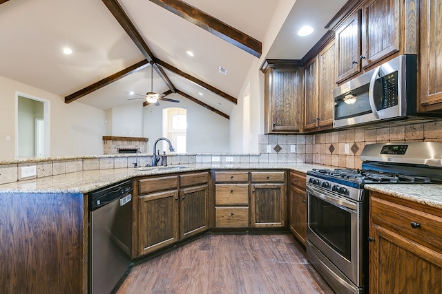 kitchen featuring dark wood-style flooring, vaulted ceiling with beams, backsplash, appliances with stainless steel finishes, and light stone countertops