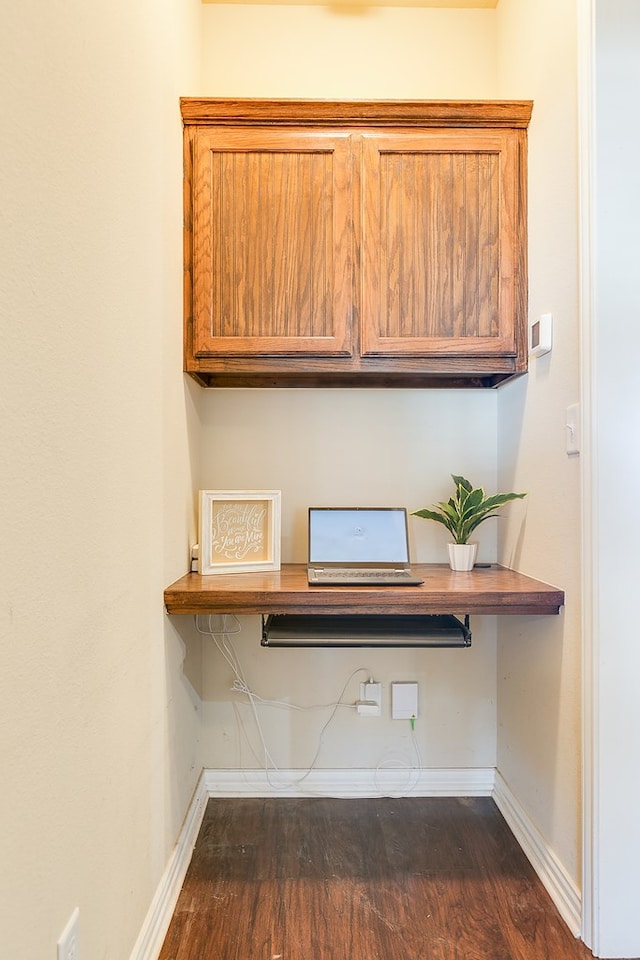 unfurnished office featuring dark wood-type flooring, built in study area, and baseboards