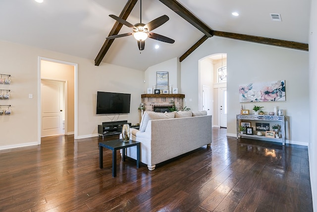 living area featuring baseboards, a ceiling fan, dark wood-style floors, beamed ceiling, and a brick fireplace