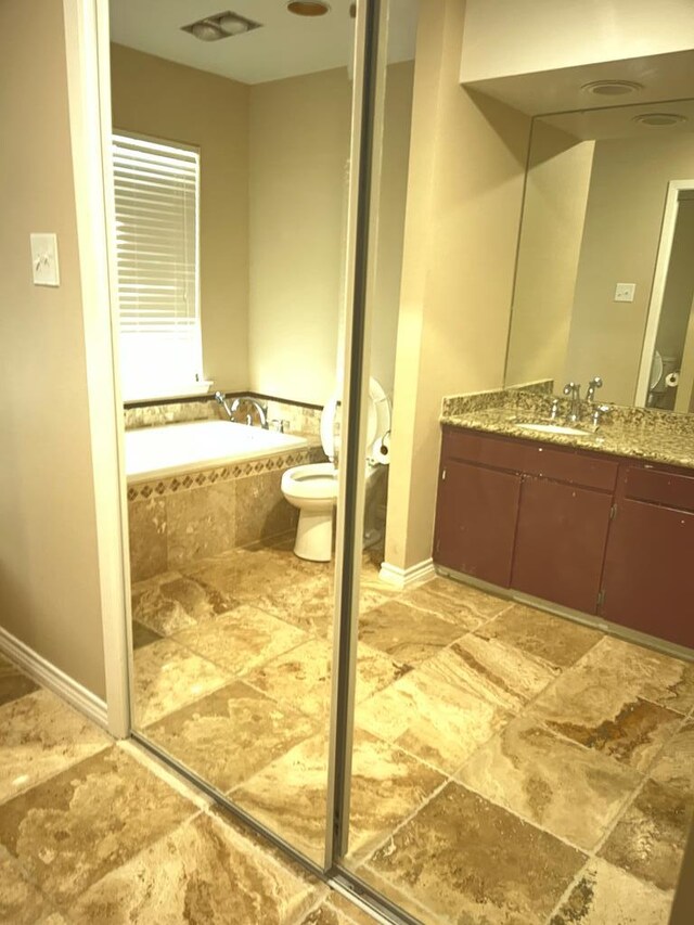 bathroom with vanity, toilet, and tiled tub