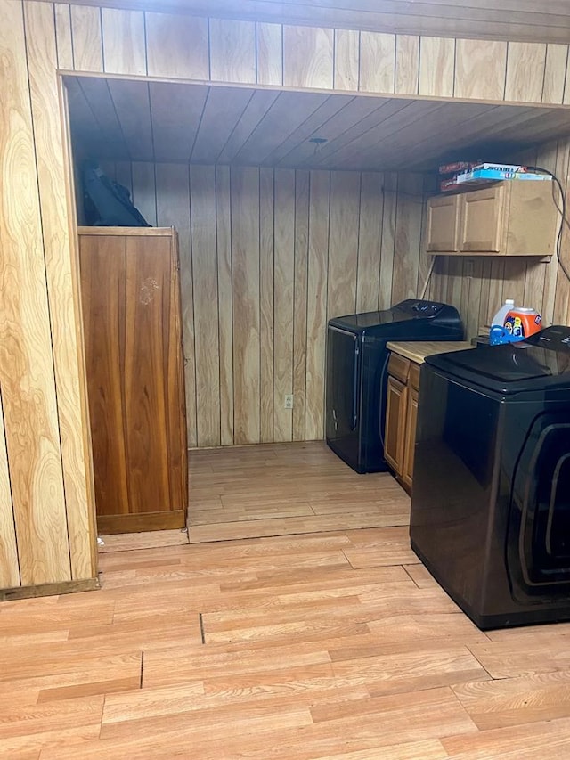 clothes washing area with cabinets, light wood-type flooring, and wooden walls